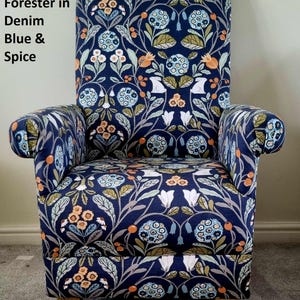 Puede incluir: Un sillón azul tapizado en una tela floral con un patrón repetitivo de flores blancas, azules, verdes y naranjas. La tela se llama "Clarke Forester in Denim Blue & Spice".