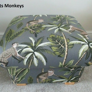 May include: A gray fabric ottoman with a monkey and palm tree print. The ottoman has wooden legs.