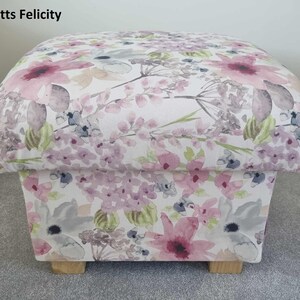 May include: A square floral patterned footstool with wooden legs. The fabric features a watercolour-style design of pink, purple, and green flowers on a white background.
