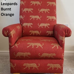 May include: A high-backed armchair upholstered in burnt orange fabric with a gold leopard print. The chair has armrests and wooden legs. The text "Fryetts Leopards Burnt Orange" is visible on the left side of the image. The chair is suitable for a living room.