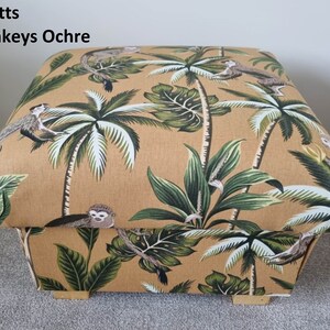 May include: A beige fabric storage ottoman with a monkey and palm tree print. The fabric has a subtle texture and the ottoman has wooden legs.