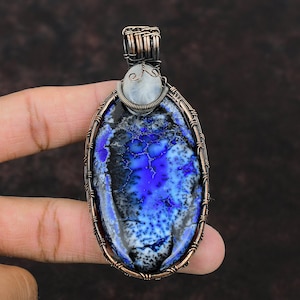 May include: A copper wire wrapped pendant featuring a blue and black agate gemstone with white accents. The pendant also has a smaller moonstone accent at the top.