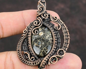 May include: A copper wire wrapped pendant featuring a green and white fossilized stone. The pendant has a detailed design with intricate wirework.