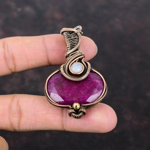 May include: A copper wire wrapped pendant featuring a large, faceted, purple gemstone and a smaller, white, round gemstone.