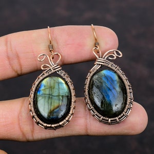 May include: A pair of copper wire wrapped earrings featuring oval-shaped labradorite gemstones. The earrings have a delicate, intricate design with a swirl at the top.