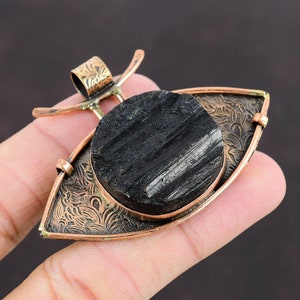 May include: A black tourmaline gemstone pendant with a copper and gold eye-shaped setting. The pendant features a detailed floral design.