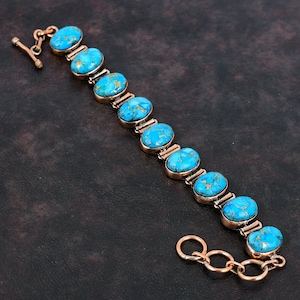 May include: A copper bracelet with a chain closure features oval-shaped turquoise stones with a marbled pattern.