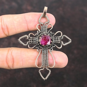 May include: A copper wire wrapped cross pendant with a pink gemstone in the centre. The cross is detailed with heart shapes at the ends of each arm.