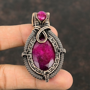 May include: A pink gemstone pendant with a copper wire wrap. The pendant is shaped like a teardrop and has a detailed wire design.