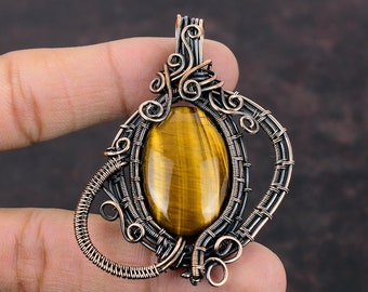 May include: A gold and copper wire wrapped pendant featuring a tiger's eye gemstone. The pendant has a unique, intricate design with swirls and loops.