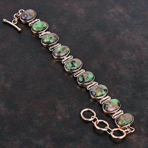 Op de afbeelding: Een koperen armband met een schuifgesp heeft ovale groene, zwarte en paarse edelstenen.