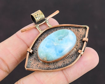 May include: A copper pendant with an oval-shaped blue and white gemstone set in a decorative frame. The pendant has a brass bail for attaching a chain.