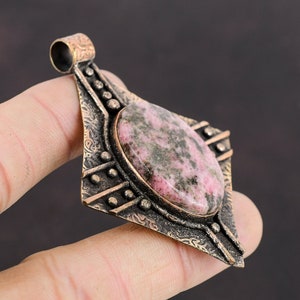 May include: A pink and green gemstone pendant with an intricate, ornate, bronze setting. The pendant is shaped like a diamond and has a detailed design.