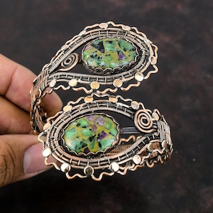 May include: A copper wire wrapped bracelet featuring two green and pink gemstone cabochons. The bracelet is adjustable and boasts a delicate, intricate design.