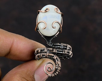 May include: A copper wire wrapped ring featuring a white moonstone cabochon. The ring is crafted in a spiral shape with a delicate wire design.