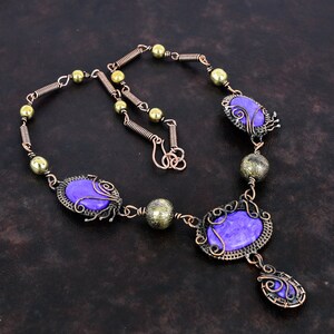 May include: A handcrafted necklace featuring purple oval-shaped stones set in ornate copper wire frames. The necklace includes brass-colored beads and a copper wire chain with a hook clasp. The design has a vintage, bohemian aesthetic.