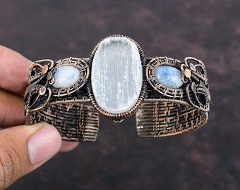 May include: A copper wire wrapped bracelet with three oval-shaped stones. The center stone is a large, white selenite stone. The two smaller stones on either side are blue moonstone.