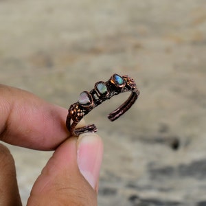 May include: A copper ring with four small, colorful gemstones set in the band. The ring is adjustable and has a rustic, handmade look.