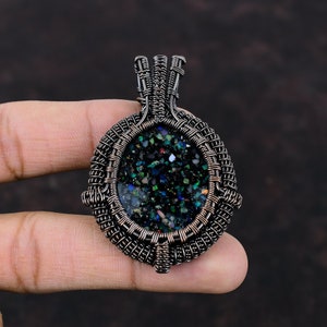 Pode incluir: Um pingente envolto em fio de cobre com uma pedra iridescente preta, verde e azul.