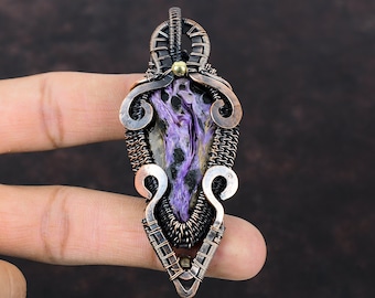 May include: A handcrafted pendant featuring a polished, teardrop-shaped stone with swirling purple and black patterns. The stone is encased in a wire-wrapped setting with copper and silver-toned metal accents. The pendant has a unique, artistic design.