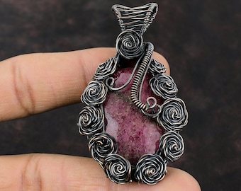 May include: A pink and purple gemstone pendant with a wire wrapped design featuring a floral motif. The pendant is made with copper wire and has a dark oxidized finish.