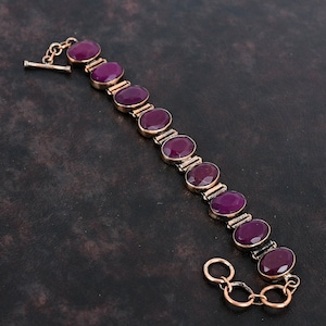 May include: A gold-coloured bracelet with oval, deep red gemstones. The gemstones are set in individual gold frames and linked together. The bracelet has a toggle clasp. The design is elegant and classic, suitable for various occasions.