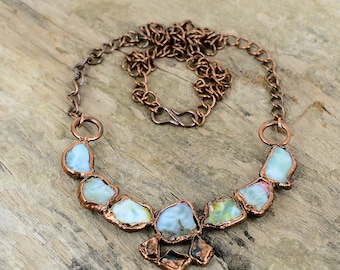 May include: A copper chain necklace with a pendant made of multiple pieces of iridescent blue and green gemstone. The pendant is shaped like a teardrop and is surrounded by a copper frame.