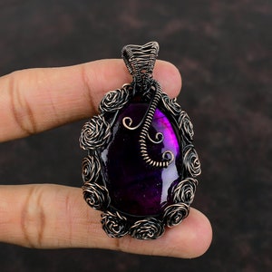 May include: A purple gemstone pendant with a wire-wrapped design featuring rose-like details. The pendant is made with copper wire and has a dark purple gemstone.
