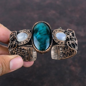 May include: A copper wire wrapped bracelet with a green gemstone and two white moonstone accents.