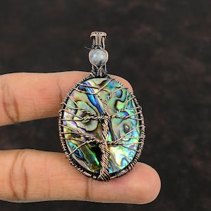 May include: A copper wire wrapped pendant featuring a tree of life design with a iridescent abalone shell inlay. The pendant has a clear crystal at the top.