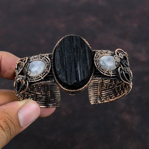 May include: A copper wire wrapped bracelet with a black tourmaline gemstone and two moonstone gemstones.