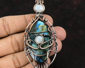May include: A copper wire wrapped pendant featuring a large oval labradorite gemstone with iridescent blue and green hues. Two smaller white moonstone gemstones are also incorporated into the design.