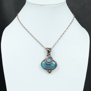 May include: A copper wire wrapped pendant necklace featuring a blue and green gemstone with a smaller blue gemstone accent. The necklace has a copper chain.