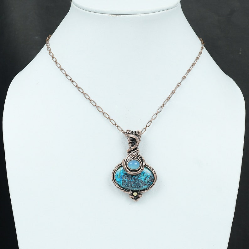 May include: A copper wire wrapped pendant necklace featuring a blue and green gemstone with a smaller blue gemstone accent. The necklace has a copper chain.