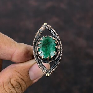 May include: A green gemstone ring with a copper wire setting. The ring is oval shaped and has a wire design that resembles an eye.