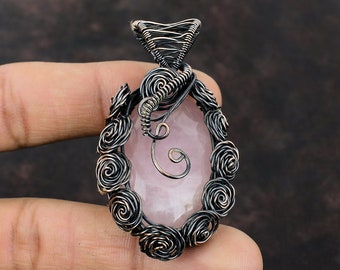 May include: A silver wire wrapped pendant featuring a rose quartz stone. The wire is twisted into a floral design with a swirl at the top.