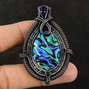 May include: A copper wire wrapped pendant featuring a iridescent abalone shell with a purple amethyst stone at the top.
