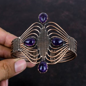 May include: A copper wire bracelet with a woven design and four amethyst gemstones. The bracelet is open and adjustable.