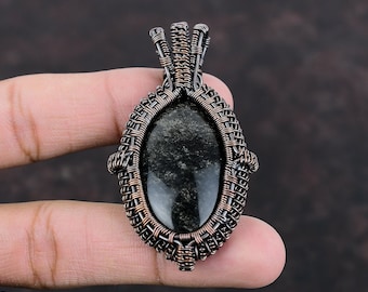 May include: An oval-shaped black obsidian gemstone pendant encased in a detailed, hand-woven copper wire frame. The dark, reflective stone is secured by intricate metal coils and loops that form a decorative border and a top bail for hanging.