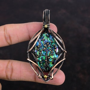 May include: A handcrafted pendant featuring an iridescent abalone shell with a tree of life design. The shell is encased in a copper wire frame with gold-coloured accents. The pendant is approximately 5 cm long.