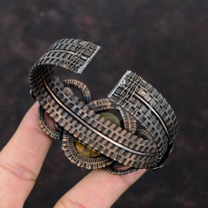 May include: A silver wire-wrapped bracelet with a woven design and a green gemstone in the center.