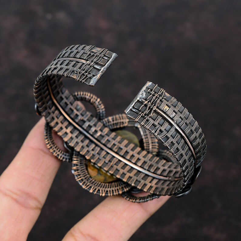 May include: A silver wire-wrapped bracelet with a woven design and a green gemstone in the center.