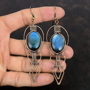 以下が含まれることがあります： 青いラブラドライトの宝石をそれぞれにつけた、長い銅線製のイヤリングのペア。イヤリングは複雑なワイヤーワークで作られており、幾何学的なデザインをしています。