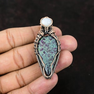May include: A copper wire wrapped pendant featuring a green and red gemstone with a white gemstone at the top.