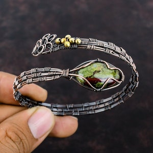 May include: A copper wire wrapped bracelet with a green and red jasper stone and gold accents.