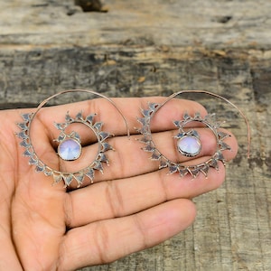 May include: A pair of silver spiral hoop earrings with a white iridescent stone in the center of each hoop.