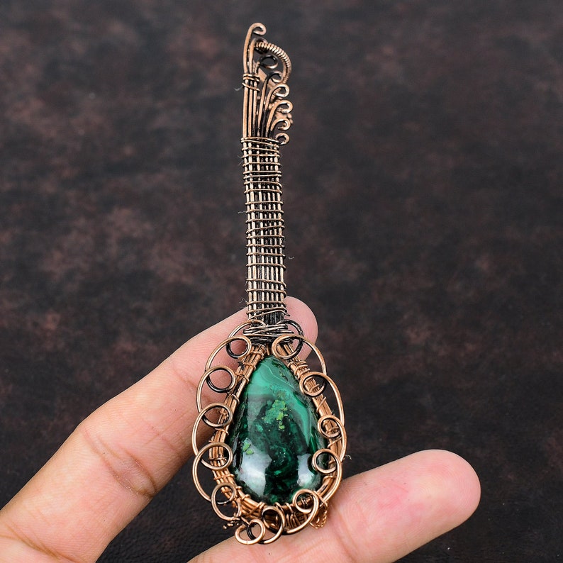 May include: A handcrafted pendant with a teardrop-shaped malachite stone, intricately wrapped in copper wire. The pendant has a long, textured handle and decorative swirls, showcasing a unique, artistic design. The malachite stone displays a rich green colour.