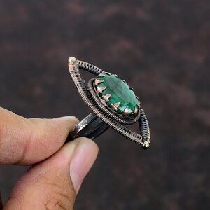 May include: A copper wire ring with a green gemstone in the center. The ring is shaped like an eye.