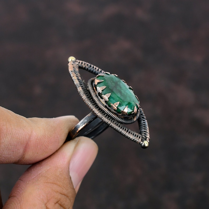 May include: A copper wire ring with a green gemstone in the center. The ring is shaped like an eye.