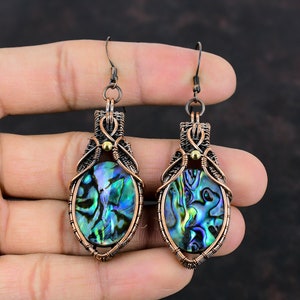 Op de afbeelding: Abalone schelpoorbellen met koperdraad. De oorbellen hebben iriserende blauwe, groene en paarse abalone schelpen in een ovale vorm, omlijst door koperdraad. Ze hebben een haaksluiting.